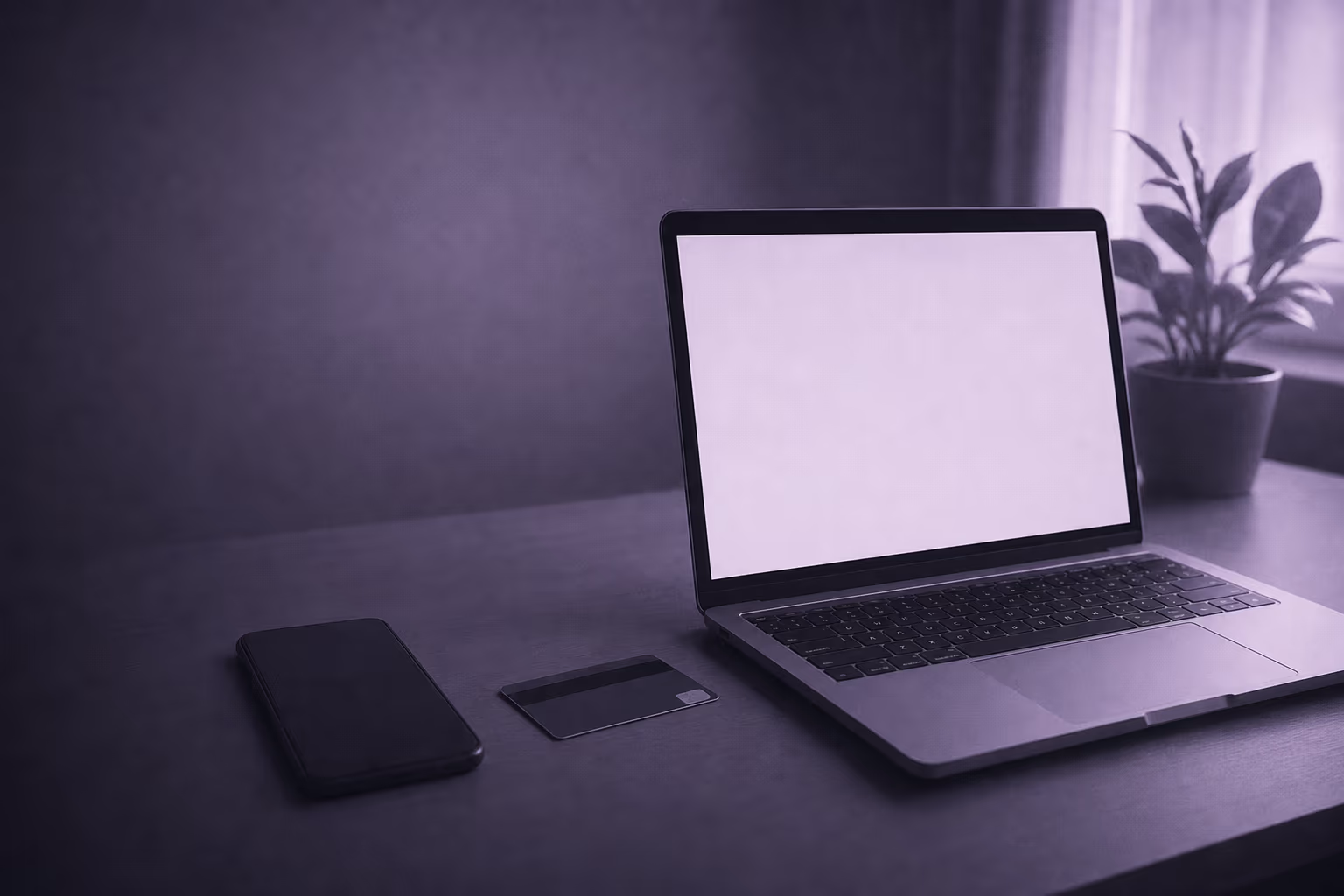 A laptop open on a desk with its screen lit, a phone face down and a bank card beside it.
