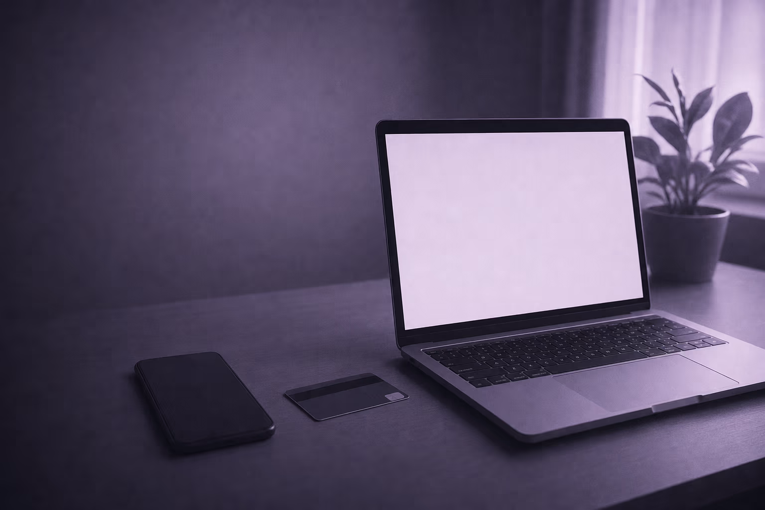 A laptop open on a desk with its screen lit, a phone face down and a bank card beside it.